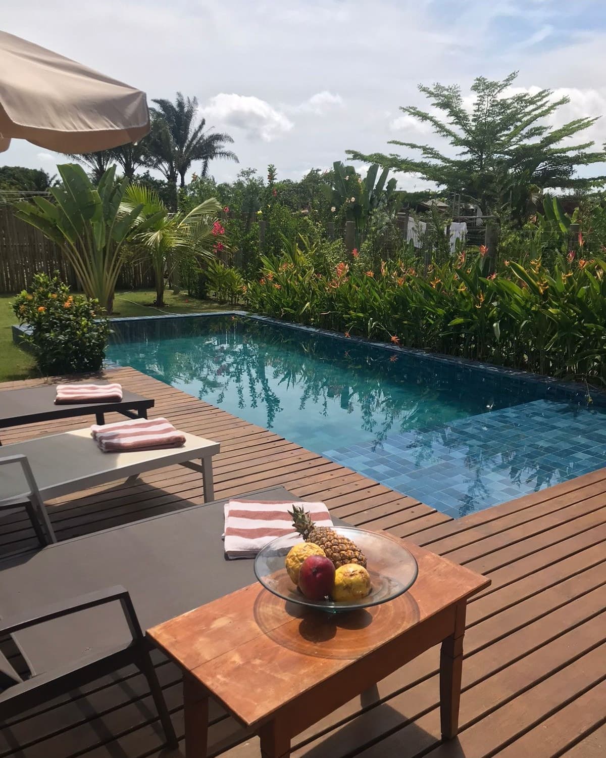 Deck de madeira com espreguiçadeiras de frente para a piscina, cercada por jardim tropical